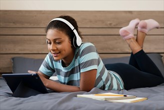 Full shot girl with tablet headphones bed