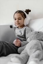 Little girl bed with headphones using tablet