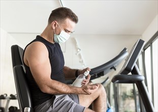 Side view man with medical mask using hand sanitizer gym