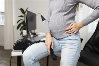 Side view pregnant businesswoman sitting desk holding phone receiver