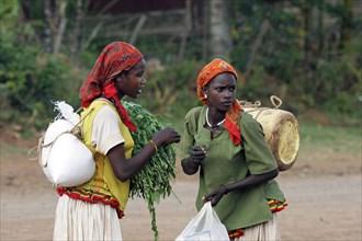 Two young women carrying merchandise on their back in street in Konso