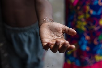 Drops of water fall on the palm of a boy's hand during a monsoon downpour
