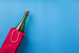 Champagne bottle bright red paper bag blue surface