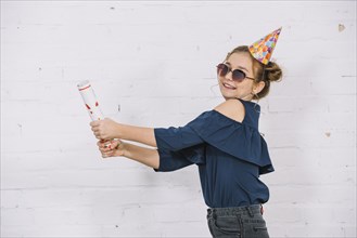 Smiling teenage girl letting off party popper standing front white wall