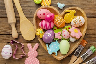Top view colorful easter eggs heart shaped plate with kitchen utensils paint brushes