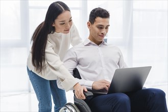 Young woman standing young man sitting wheelchair using laptop