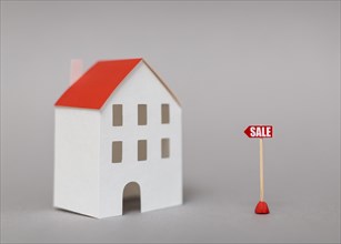 Sale post near miniature house model against gray background