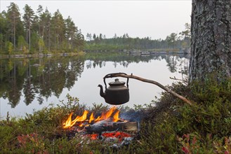 Blackened tin kettle boiling water over flames from campfire during hike along lake