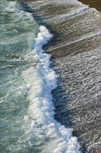 Wave in the surf crashing on sandy beach along the seashore coast