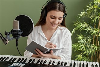 Front view smiley female musician playing piano keyboard writing songs while recording
