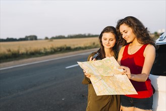 Women standing near white car looking map
