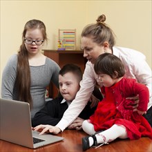 Woman showing children with down syndrome something laptop