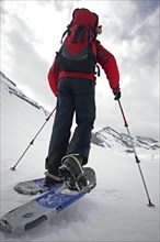 Close up of mountaineer with backpack wearing snowshoes while snowshoeing in deep powder snow in the mountains in winter