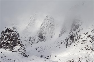 Snow covered rock face in the fog along the fjord Raftsund in winter