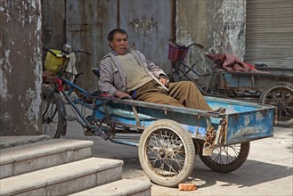 Driver of bicycle cart smoking cigar in opium pipe