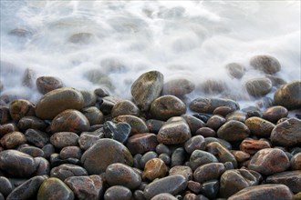 Close up of colourful pebbles covered by wave on shingle beach at rising tide