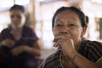 Old Burmese woman of the Bamar tribe wearing thanaka and smoking a cigar in Kayin village near Hpa-an