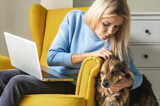 Woman working laptop from armchair during pandemic petting her dog