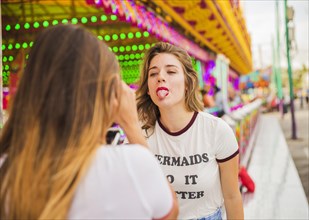 Rear view woman taking her friend showing tongue amusement park