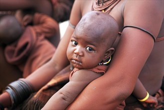 Close up of baby in mother's arms of the Himba tribe with red skin covered in otjize