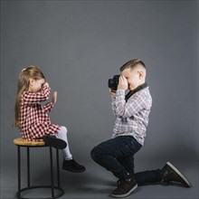Side view boy taking girl sitting stool with camera