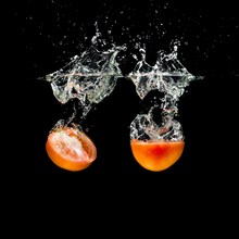 Two halves tomatoes splashing into clean water