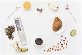 Rolled up newspaper with coffee cup croissant fruits white background