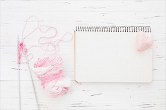 Pink yarn with crochet beside notepad heart wooden background