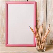 White blank frame with pink border colored pencils glass holder wooden desk