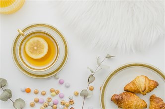 Fur baked croissant candies ginger lemon tea cup white background