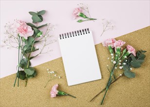 Overhead view spiral notepad surrounded with gypsophila carnation flowers dual pink cardboard background