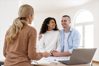 Happy embraced couple conversing with female realtor