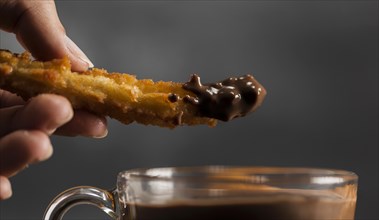 Hand dipping fried churros chocolate close up