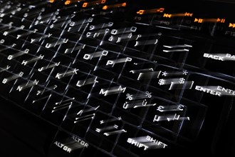 Blurred black computer keyboard with illuminated backlit white keys