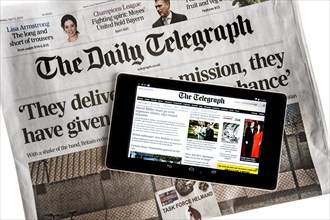 Touchscreen digital tablet showing online news on top of British The Daily Telegraph newspaper on white background