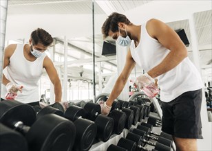 Side view man disinfecting gym equipment while wearing medical mask