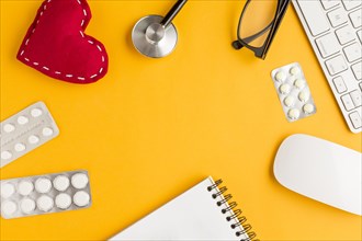Arrangement blister packed medicines stitched heart shape spiral notepad wireless keyboard mouse spectacles stethoscope yellow backdrop