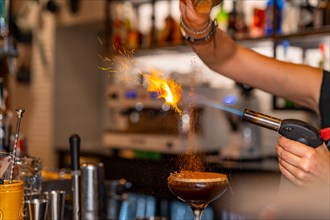 Close-up photo of an unrecognizable bartender burning the topping of a cocktail using torch