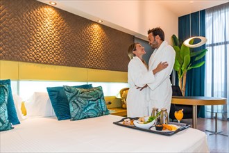 Couple standing on a luxury hotel room with breakfast on the bed