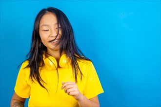 Studio photo with blue background of a young casual happy chinese woman with headphones dancing