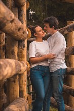 Vertical photo of a couple standing embraced together between wood rails in the countryside