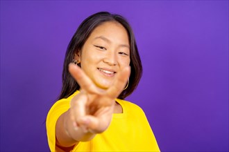Studio photo with purple background of a chinese woman gesturing victory smiling at camera
