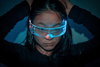 Close-up studio photo with blue background with neon lights of a chinese young woman using augmented reality goggles