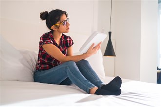 Side view of a young woman sitting comfortable reading a book in an hotel