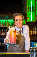 Vertical portrait of a happy bartender serving a luxury cocktail in the counter of a bar