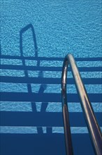 Water surface with light reflections and railing in a swimming pool