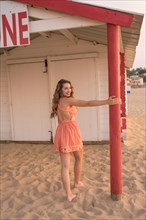 Sensual woman walking and holding onto a post of a house on the beach