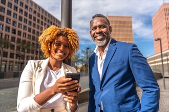 Smiling african business people using phone outdoors in the city street