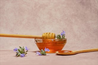 Natural honey in a glass bowl with a wooden spoon and fresh rosemary sprigs in bloom