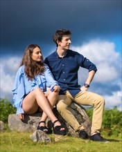 Vertical photo of young elegant couple gazing the horizon sitting on a hill